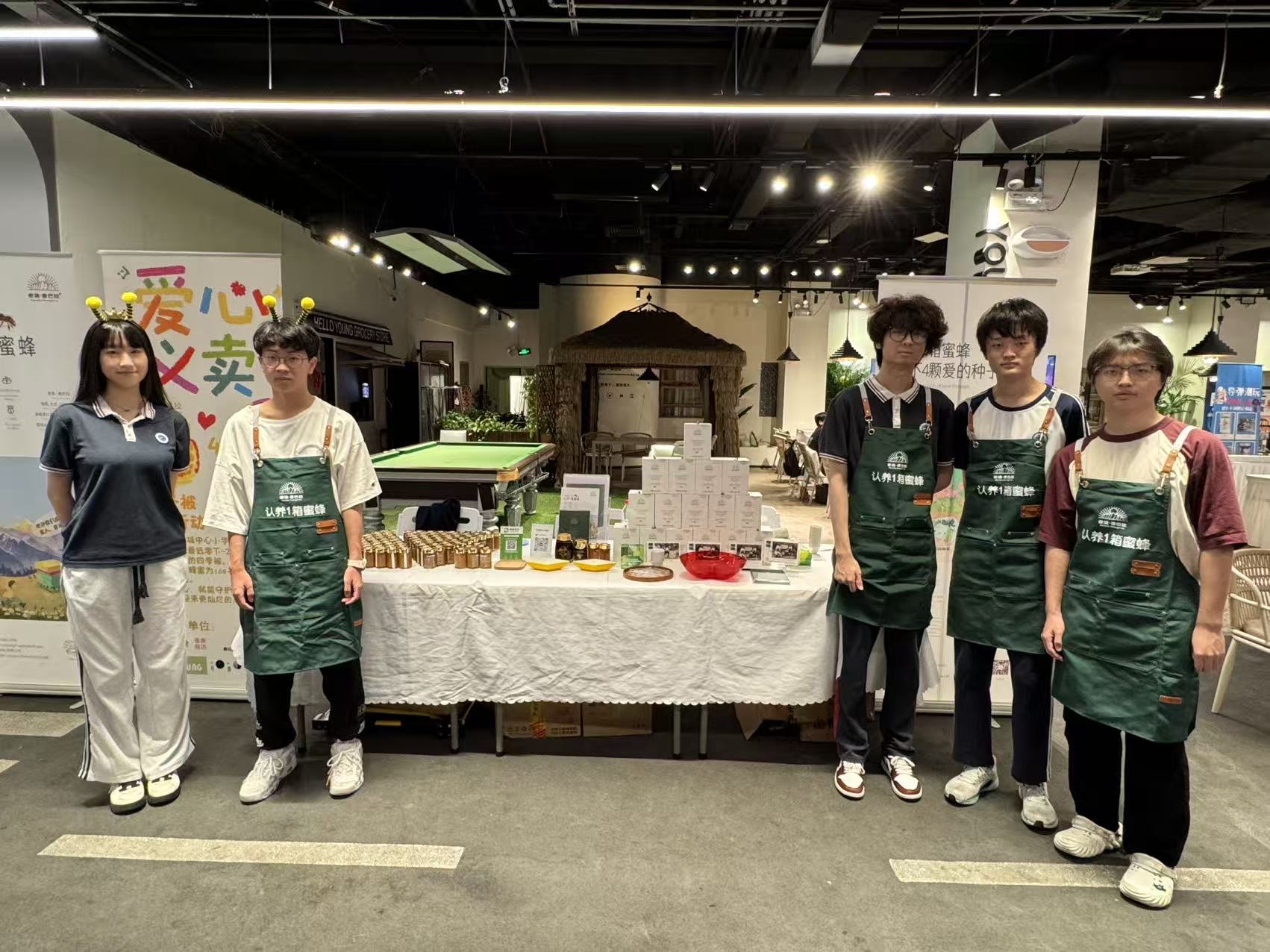 Five student volunteers wearing the initiative's green charity-sale aprons behind the booth table